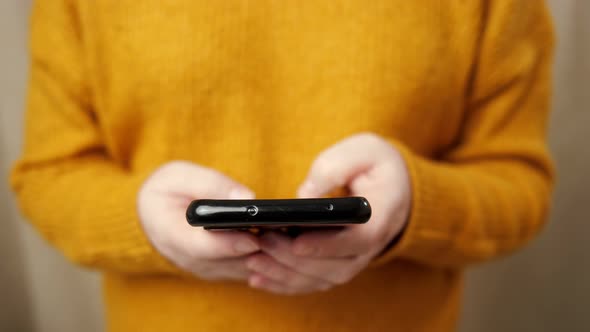 Young Woman in Pullover Hands Type on Black Smartphone alt