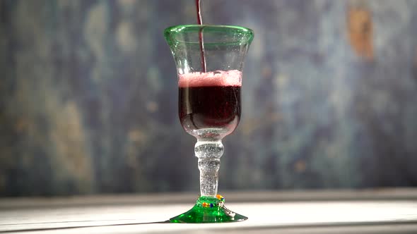 Seamless, looping clip of red wine pouring into a rustic glass with blue background. alt