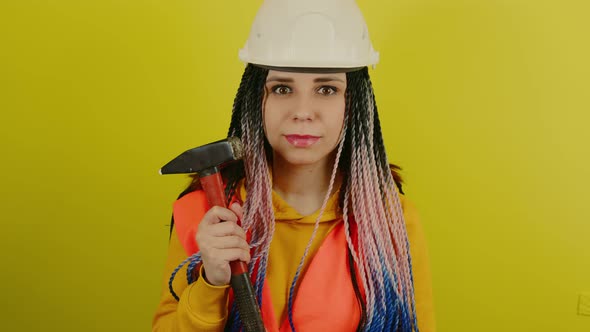 Female Construction Worker in Overalls with Hammer on Yellow Background in Studio alt