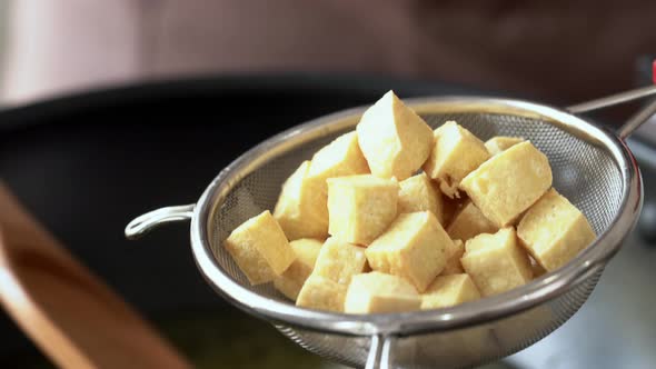 Chef draining cooked tofu cubes in kitchen strainer