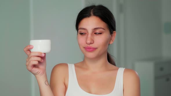 The Girl Holds a Face Cream in Her Hand and Looks at It Showing That She Does Not Like It