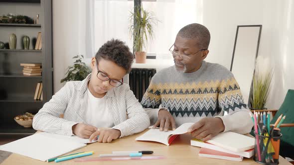 Caring African American Grandfather Helping His Clever Grandson with Homework Sitting Together at alt