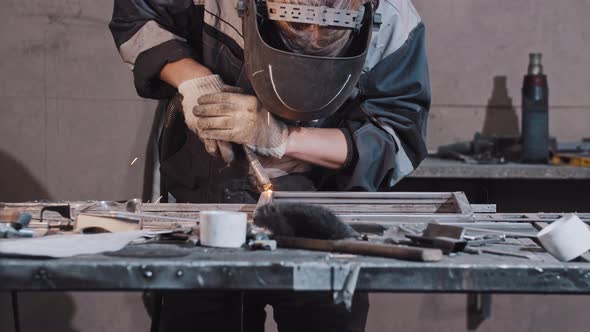Young Man Worker in Protective Gloves and Helmet Welding Parts of the Metal Detail Together alt