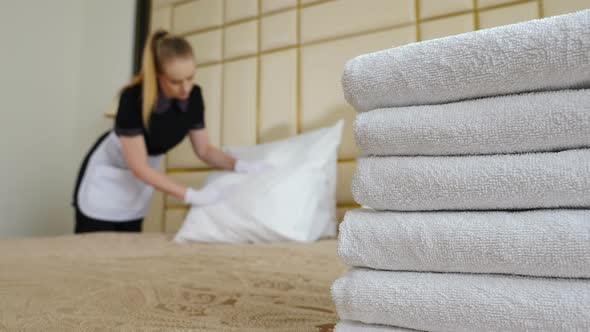 Hotel Concept. Young, Beautiful Maid in Uniform and Apron Making Bed in Room, Shot Through Stack of alt