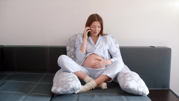 Smiling pregnant woman talking on the phone at home on the sofa