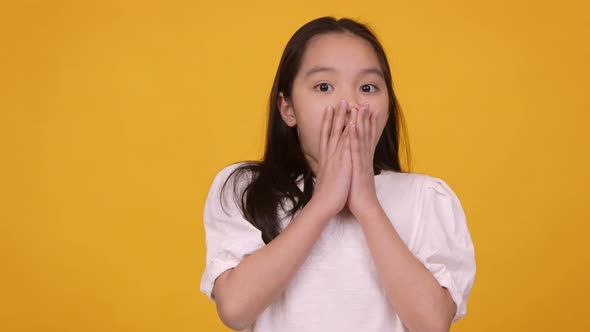 Shocked Little Asian Girl Feeling Surprised Closing Her Mouth in Amazement Orange Background alt