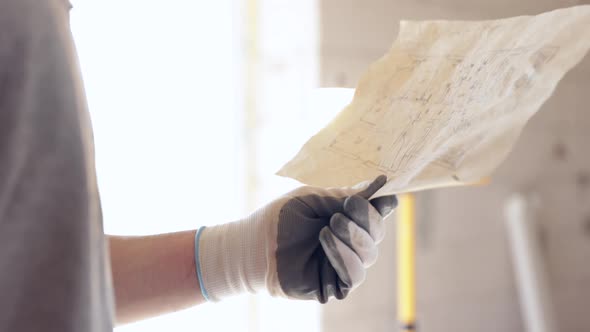 A man builder looks at a construction drawing in a building. alt