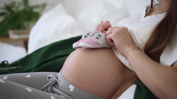 Pregnant Woman at Home Lying on Bed and Put Baby Footwear on Belly Walk on Tummy Spbd alt