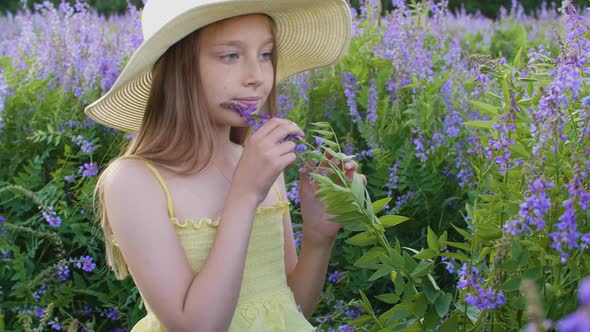 Adorable Teenage Girl in Hat Sniffing Flowers on Green Meadow alt
