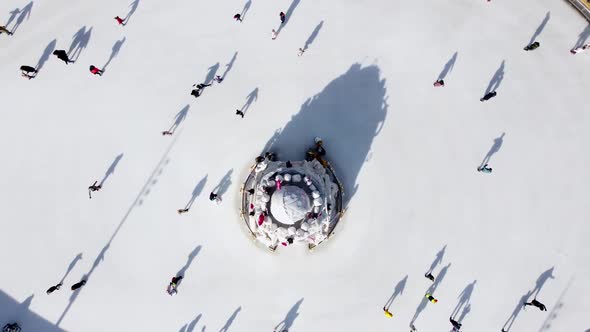 Many People are Skating on White Outdoor Ice Rink in City on Sunny Winter Day alt
