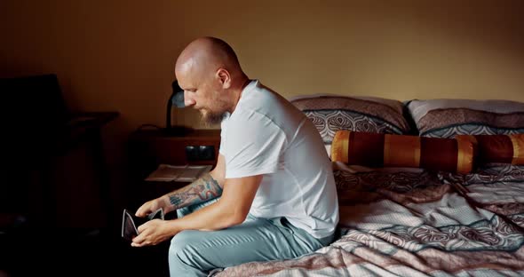 Man Sitting on Bed Looking at Empty Wallet. Male Very Dissapointed and Depressed Feelling Hopeless alt