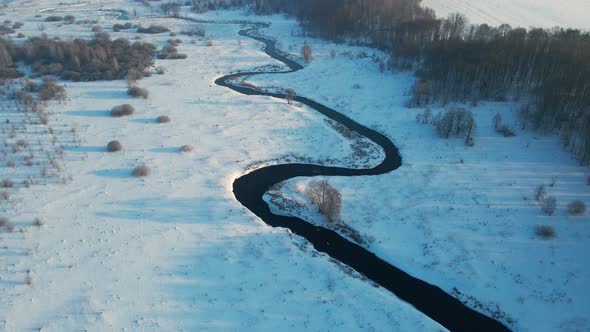 winter river winding in the middle of the forest and fields view from the drone 4k video alt