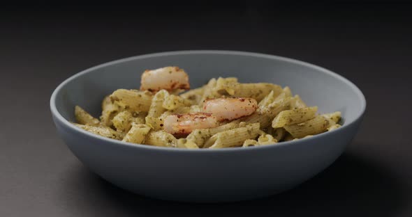 Slow Motion Fried Shrimps Fall on Pest Penne in Blue Bowl on Black Background alt