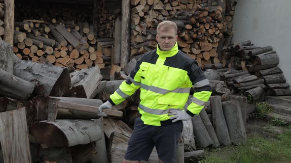 Lumberjack in Reflective Jacket. Man Woodcutter Hold Huge Axe Show Ok Sign. Sawn Logs, Firewood alt
