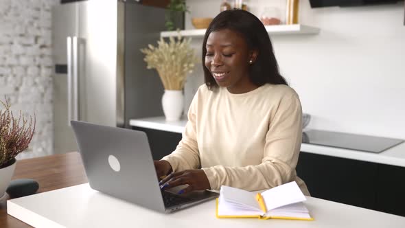A Beautiful AfricanAmerican Woman in Casual Wear is Using Laptop Computer Sitting in Home Office
