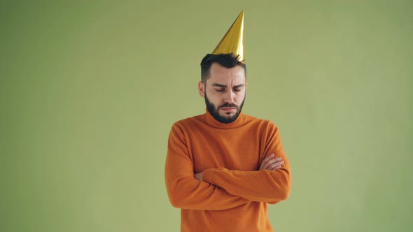 Portrait of Upset Man in Party Hat Standing Alone with Arms Crossed Sighing alt