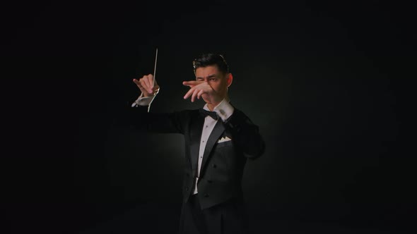 An Orchestra Leader Wearing Suit Using the Conducting Baton to Synchronize the Musicians alt