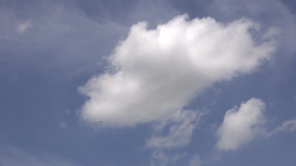 An airplane flies across a blue sky with white fluffy clouds.