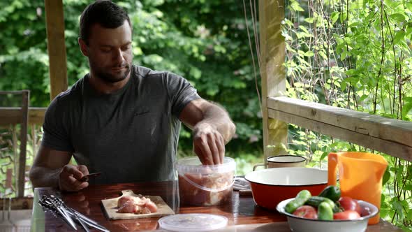 Man is Cutting Marinated Meat for Cooking on Grill Putting Pieces on Skewers alt