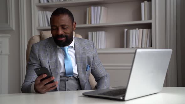 Happy African-American Bearded Man in a Gray Suit, White Shirt. The Businessman Is on the Desktop at alt