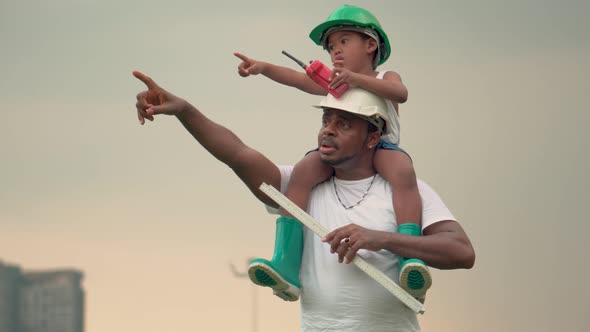 Cheerful African American father and son in hard hat, Happy dad carrying son on shoulders