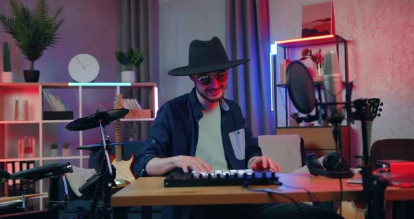 Bearded Guy in Hat and Glasses which Sitting at His Workplace in Home Studio and Playing alt