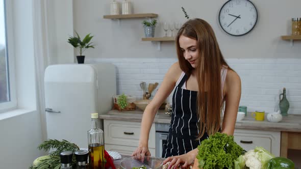 Vegan Girl Cooking Salad with Raw Vegetables While Looking on Mobile Phone for Online Recipe alt