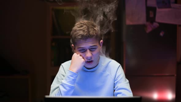Smoke comes from a young guy who works at a computer in the middle of the night alt