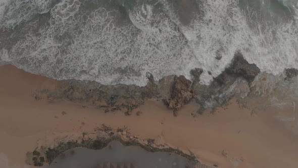 Top-down static shot over ocean waves crashing on Ponta da Calheta beach, Porto Santo island alt