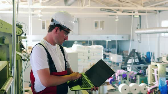 Factory Worker Using His Laptop To Monitor Plastic Bag Production Process alt