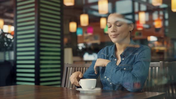 View Through a Glass Showcase of a Young African American Woman Enjoying Aromatic Coffee in Mall alt