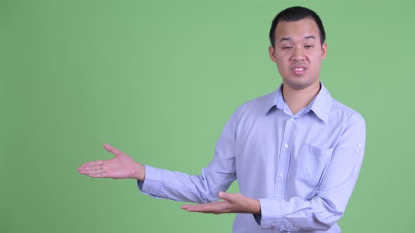 Stressed Asian Businessman Talking While Showing Something alt