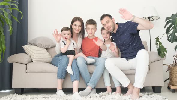 Happy European Family Relaxing on the Couch at Home They Cheerfully Wave Their Hands at the Camera alt