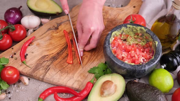Making Guacamole Sauce  Woman Slicing Chili Pepper on a Wooden Cutting Board alt
