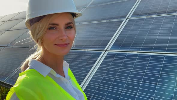 Professional Woman Worker Engineer Wearing a White Hard Hat Standing Near a Solar Farm Smiling at