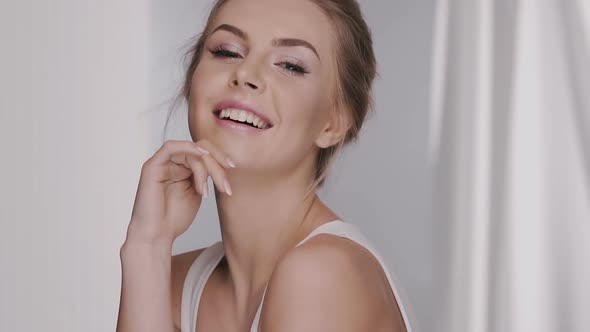 Attractive Female with Naked Shoulders Smiles and Moves with White Curtains on Background alt