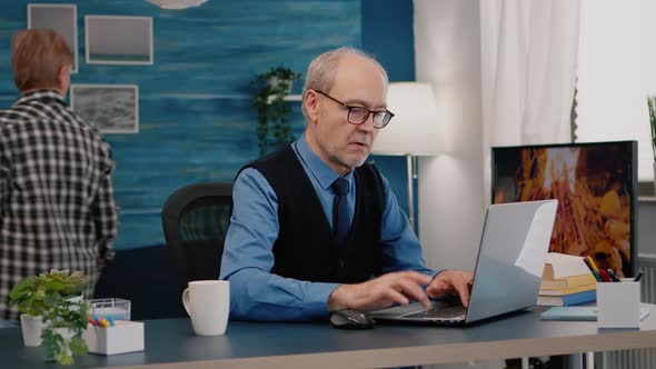 Focused Old Entrepreneur Checking Graphics Writing on Laptop alt