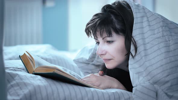 Middleaged Pretty Brunette Woman Lies In Bed And Attentively Reads A Book Cinematic