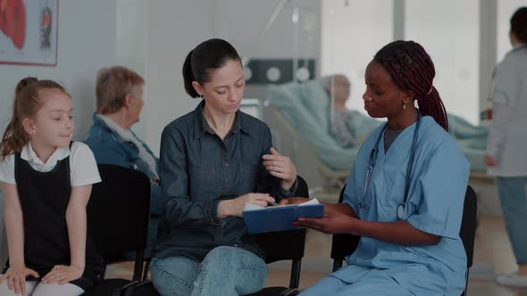 Mother with Child Signing Checkup Papers in Waiting Room alt