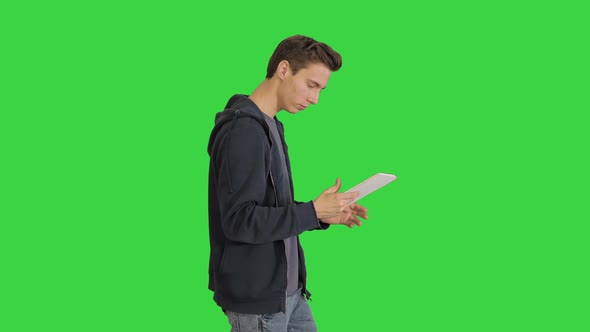 çYoung Man Using Digital Tablet While Walking on a Green Screen, Chroma Key. alt