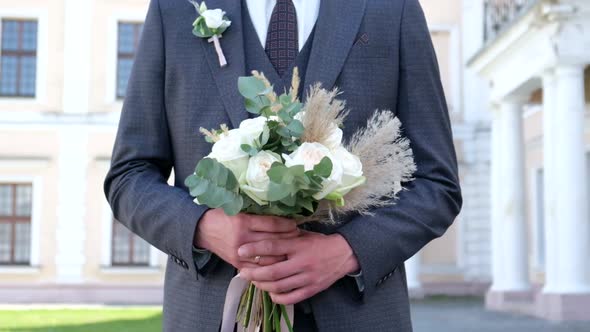 Close Up of Young Stylish Groom Hands Holding Beautiful White Wedding Bouquet alt