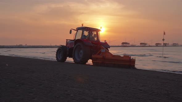 A tractor cleans the sand of the beach at sunrise alt