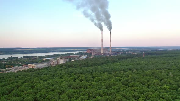 Aerial view on the green forest and pipes with smoke from plant. alt