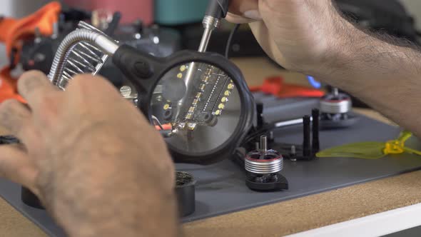 Technician Solders Wire to Drone Chip on Grey Plastic Tray