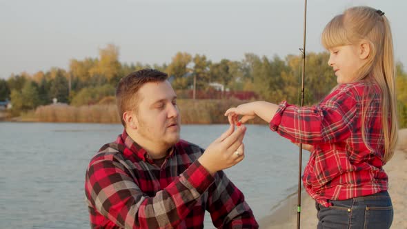 Father Showing Fish Bait To Daughter Near Lake