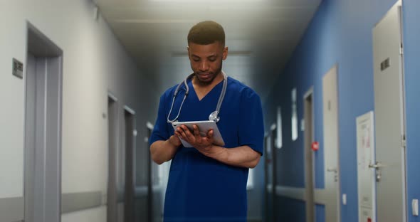 African American Doctor Uses a Tablet Standing in Corridor of Medical Center alt