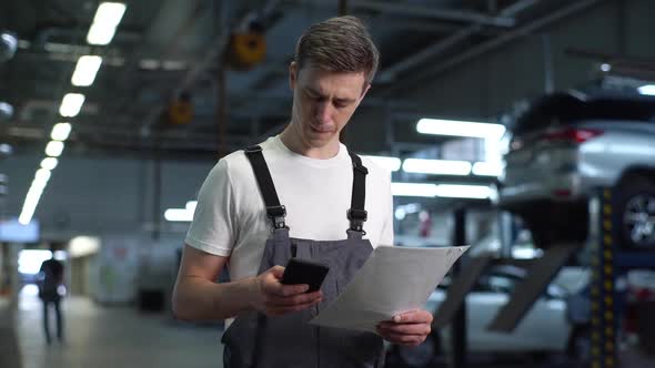 Portrait of Serious Handsome Mechanic Male in Blue Uniform Dialing Customer Number for Call alt