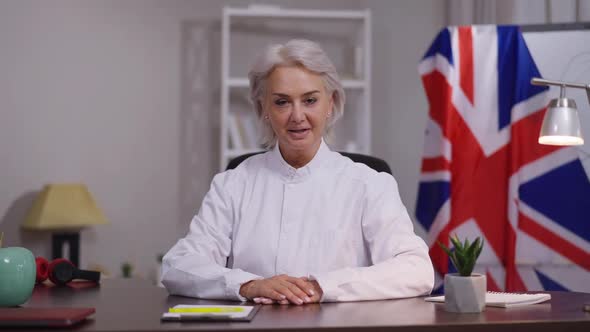 Front View Confident Female Mature Business Blogger Sitting at Table Talking in Slow Motion with UK alt