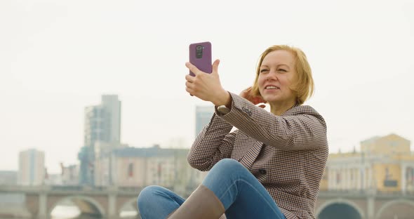 Online Dating Concept 40 Year Old Woman Sits on the Street with a Phone and Chats Animatedly with alt