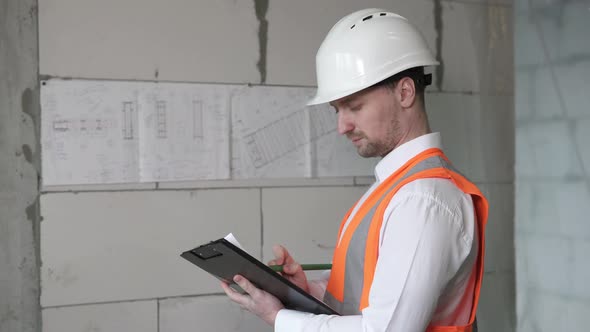 Work with the drawings of a civil engineer at a construction site. The construction foreman is worki alt